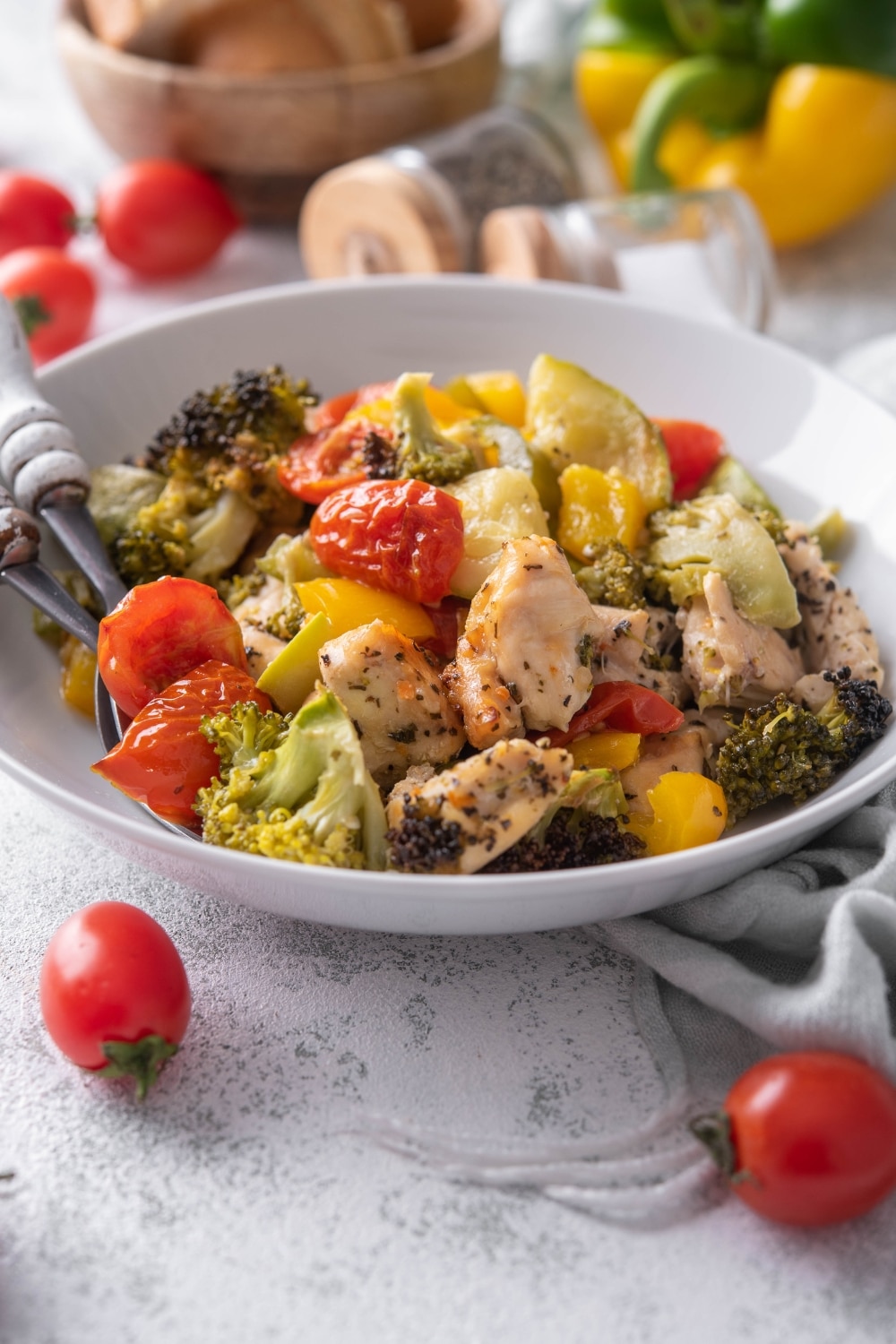 Roasted chicken and veggies in a shallow white bowl with two forks.