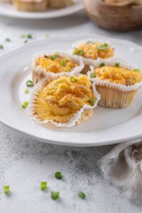 Four sausage egg muffins in muffin liners on a white plate, one partially opened.