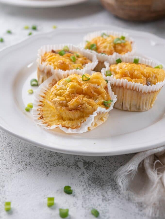 Four sausage egg muffins in muffin liners on a white plate, one partially opened.