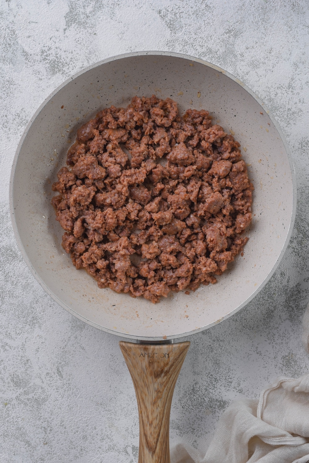 Ground Italian sausage in a white skillet with a wooden handle.