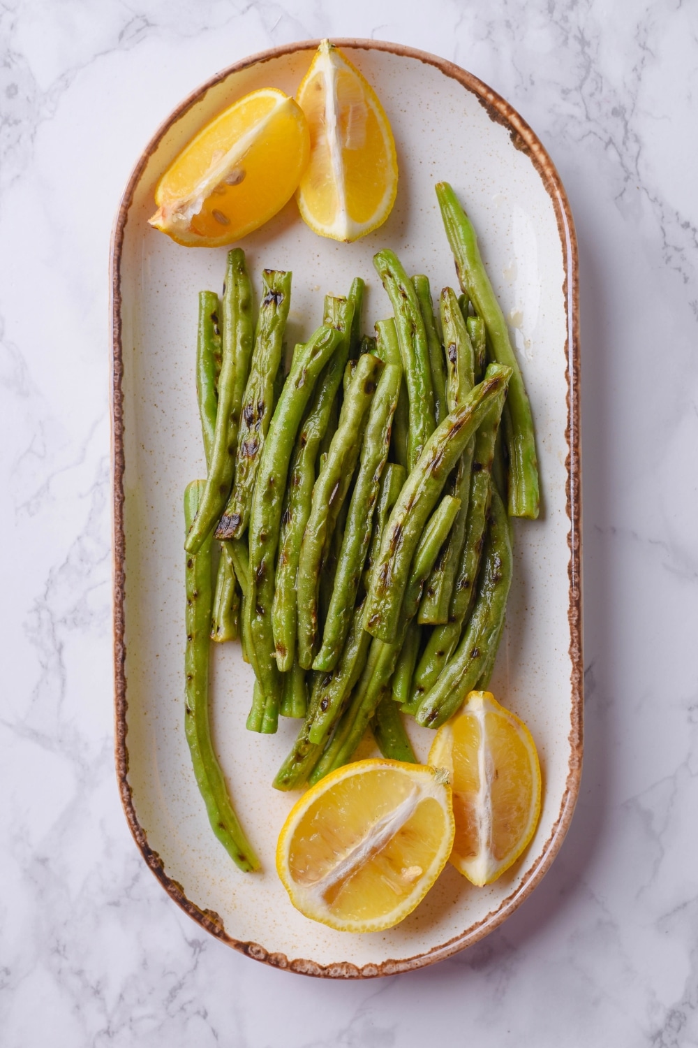 A bunch of grilled green beans on a plate with lemon wedges.