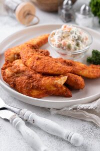 Baked chicken tenders on a plate served with a small bowl of creamy potato salad.