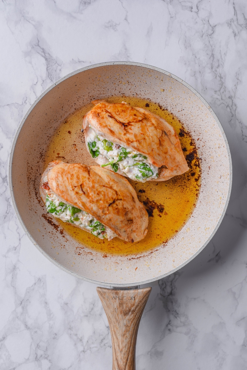 Two cooked stuffed chicken breasts in a skillet with oil.