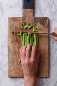 A hand holding green beans and cutting off the tops.