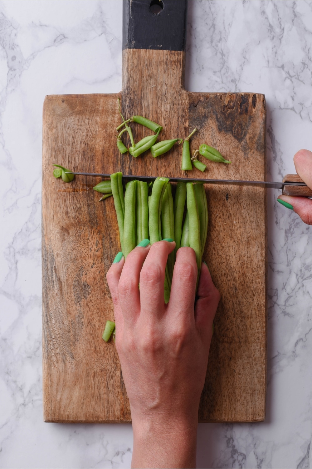 A hand holding green beans and cutting off the tops.