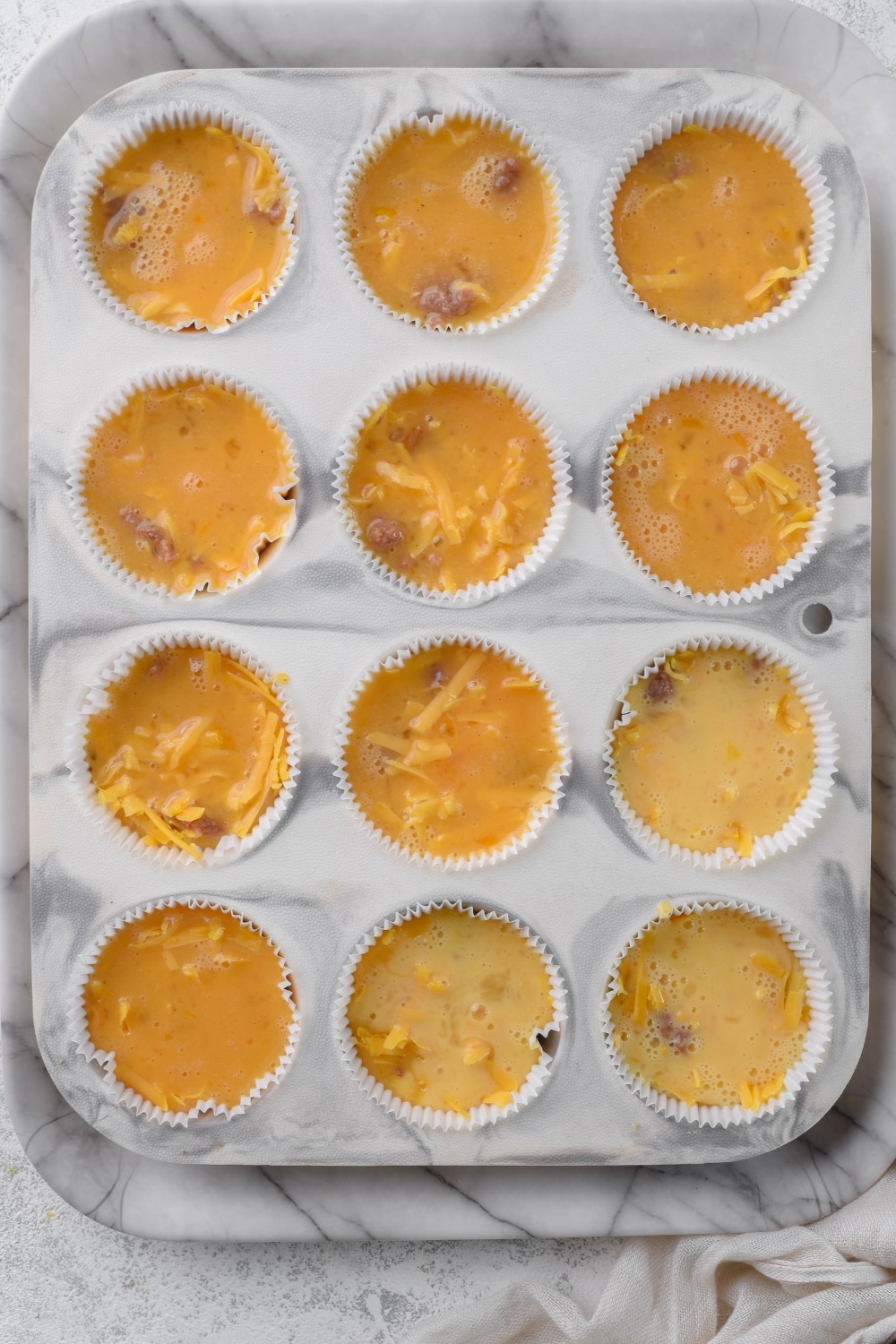 A 12-cup muffin tin with liners filled with sausage egg muffin batter.