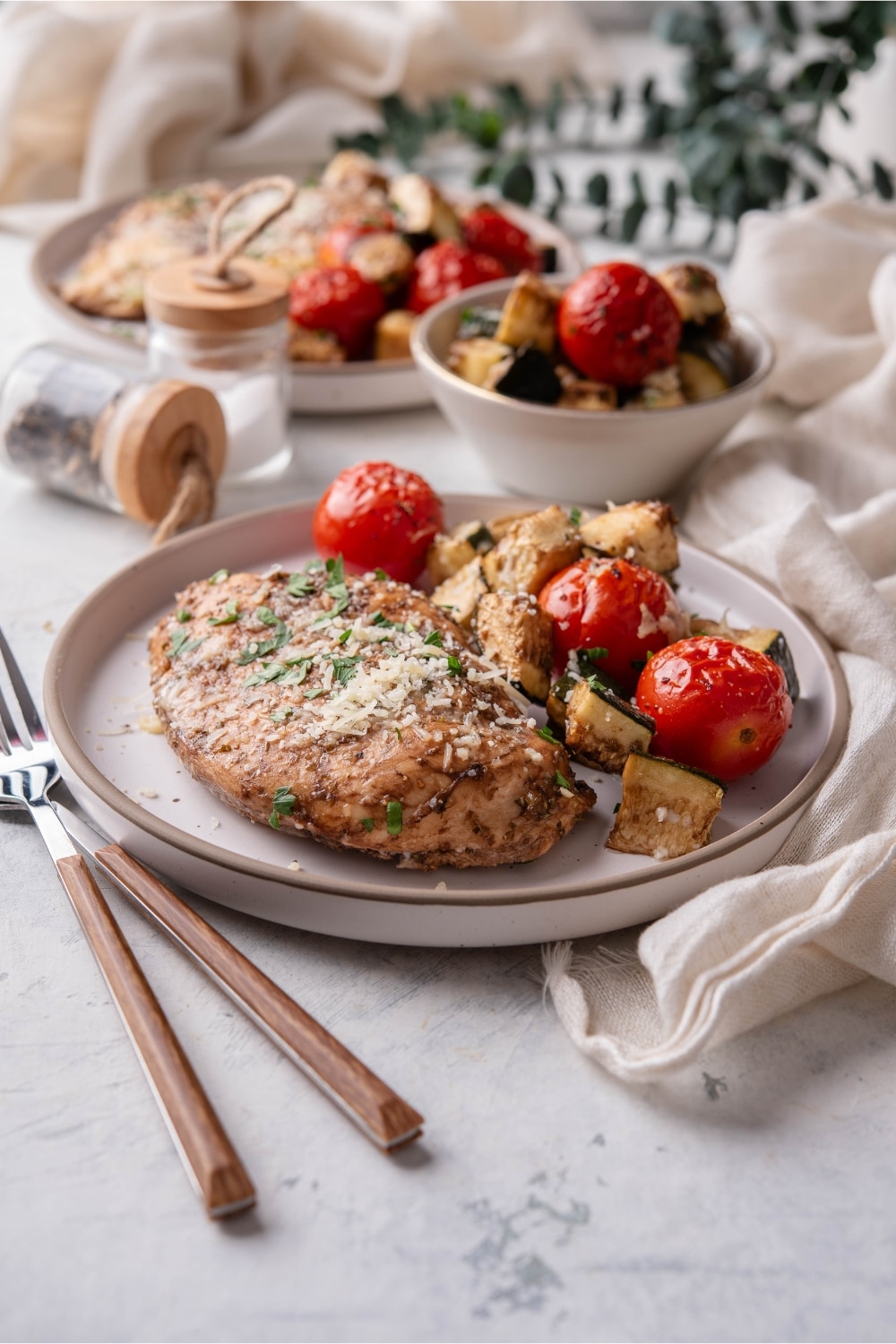 A plate of baked Italian chicken with roasted cherry tomatoes and zucchini.