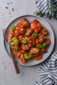 Top view of a plate of Szechuan chicken with peppers, served with a fork.