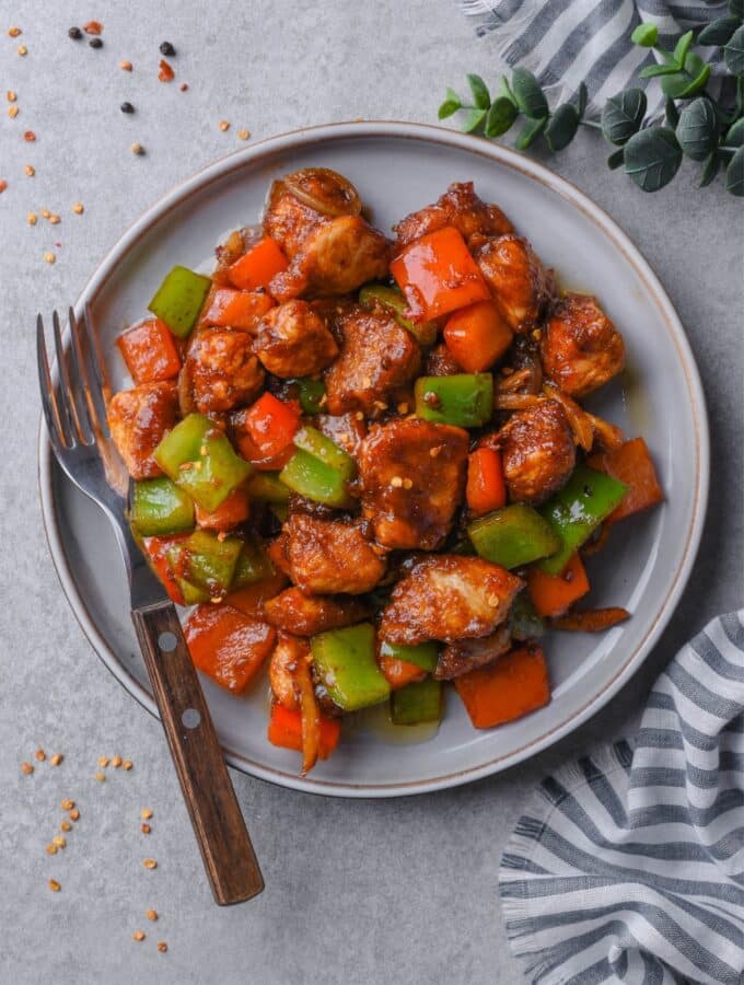 Top view of a plate of Szechuan chicken with peppers, served with a fork.