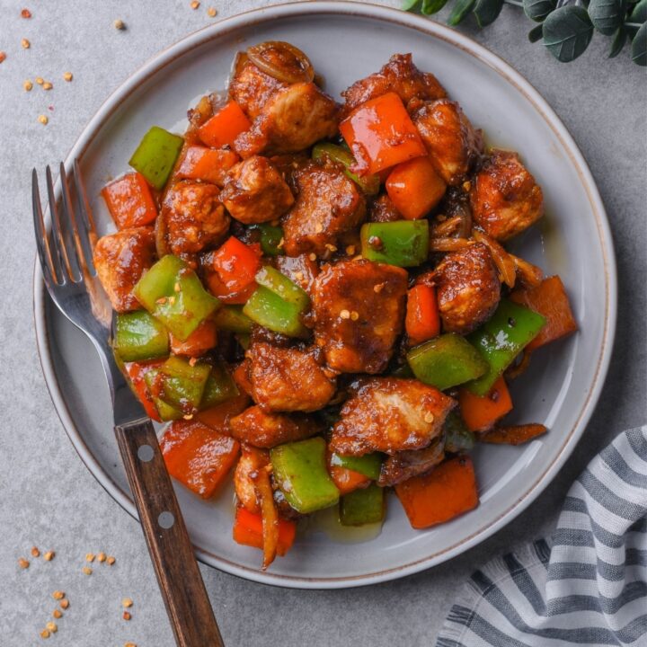 Top view of a plate of Szechuan chicken with peppers, served with a fork.