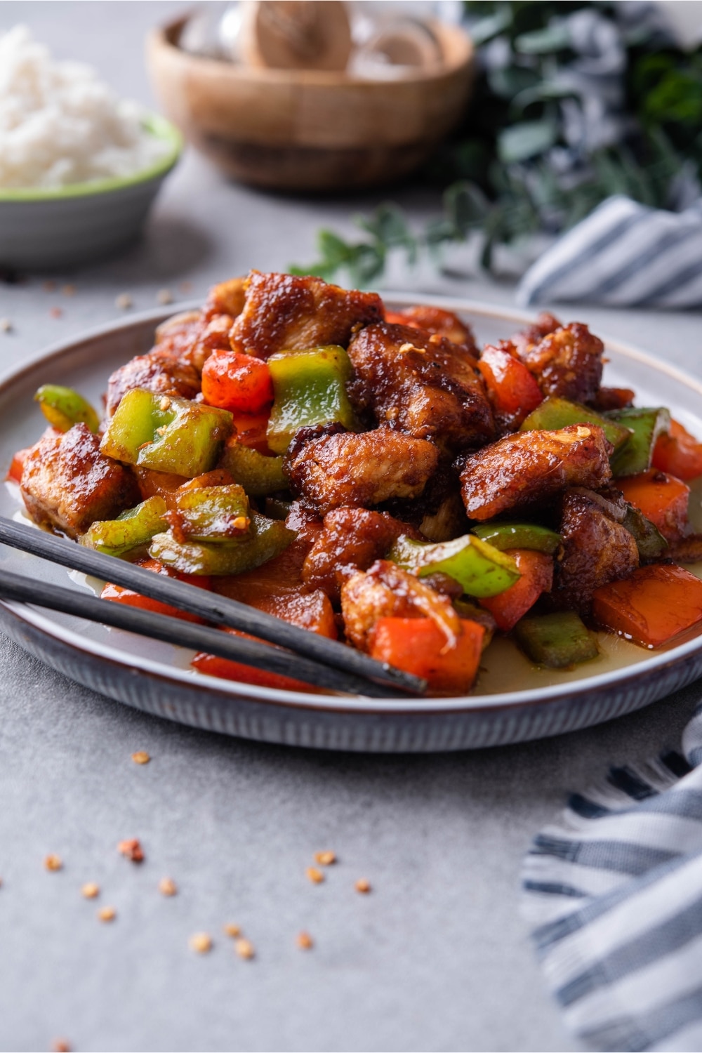 Szechuan chicken with peppers served on a plate with a pair of chopsticks.