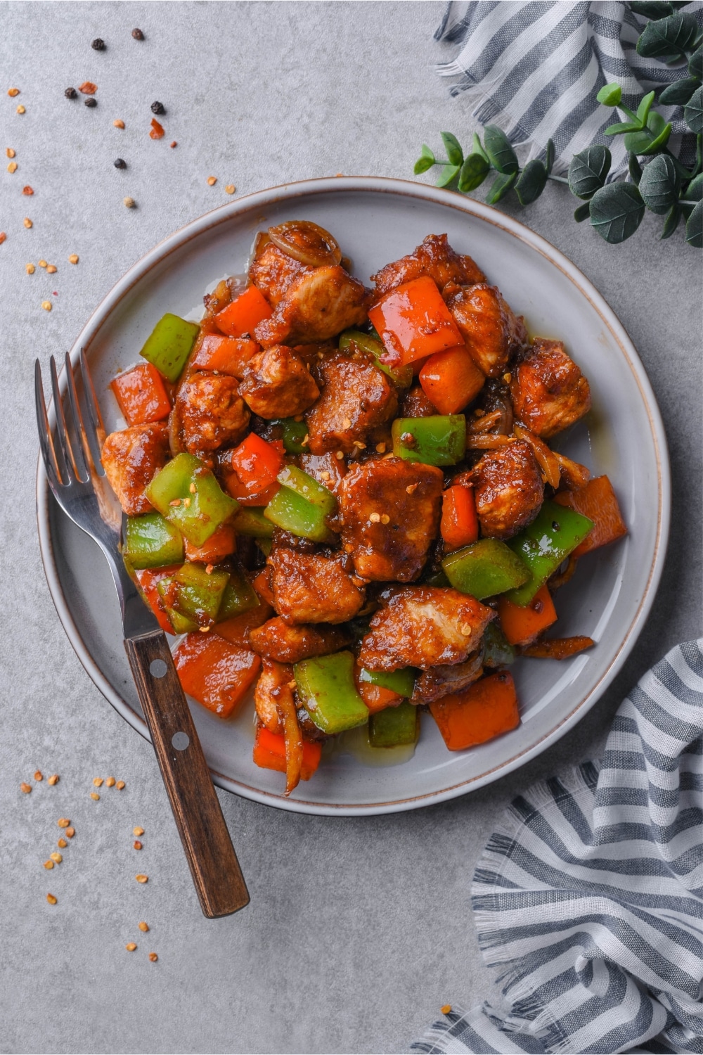 Top view of a plate of Szechuan chicken with peppers, served with a fork.