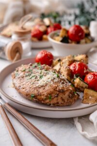 A plate of Italian baked chicken served with roasted tomatoes and zucchini.