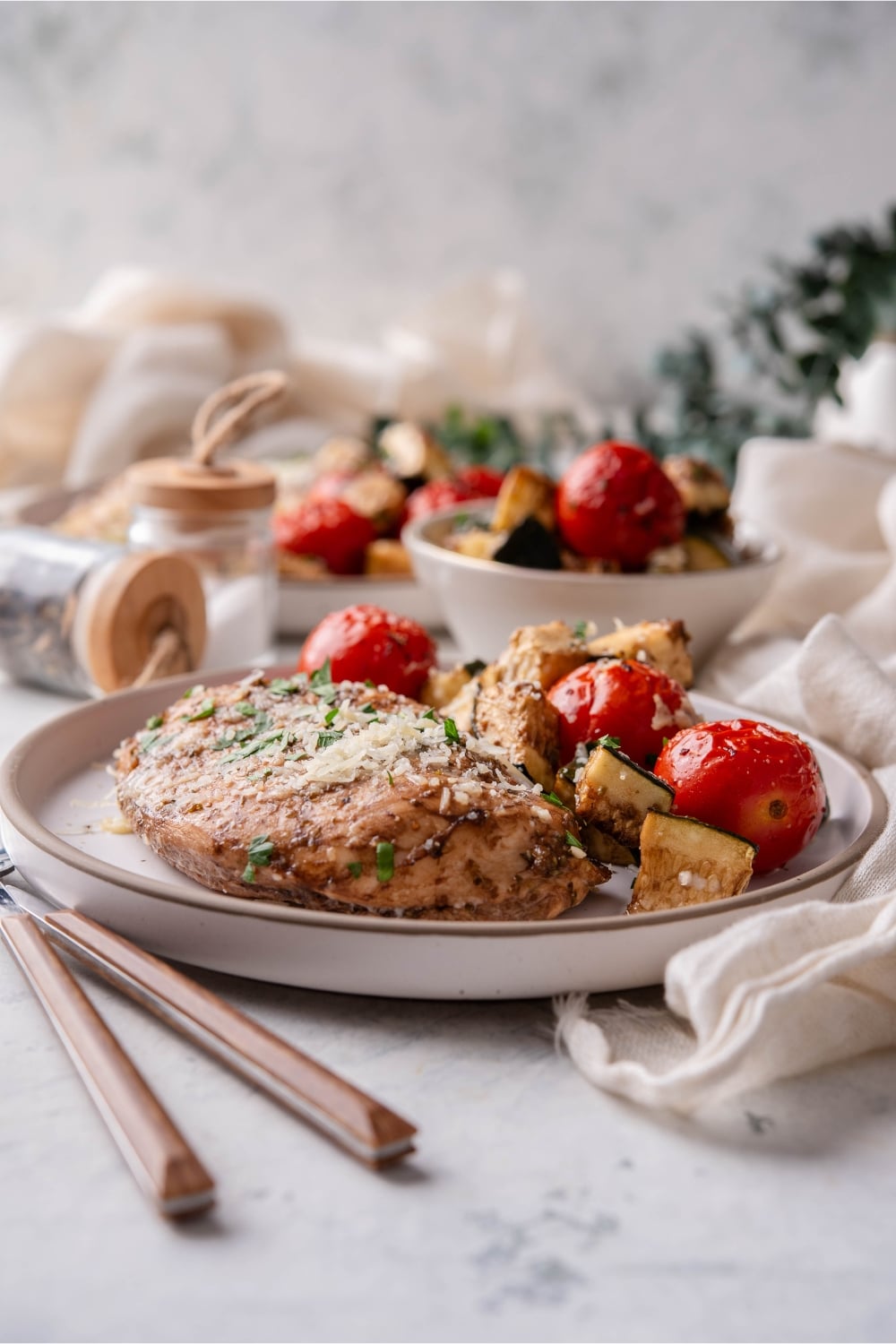 Italian baked chicken on a plate with roasted tomatoes and zucchini.