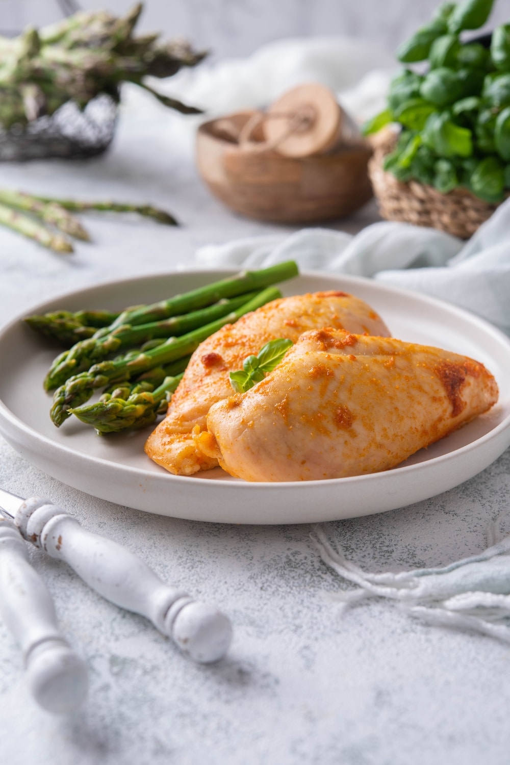 Baked chicken breast on a plate, garnished with basil leaves and served with asparagus.