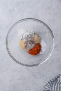 A glass bowl of baking powder, paprika powder, garlic powder, salt, and pepper.