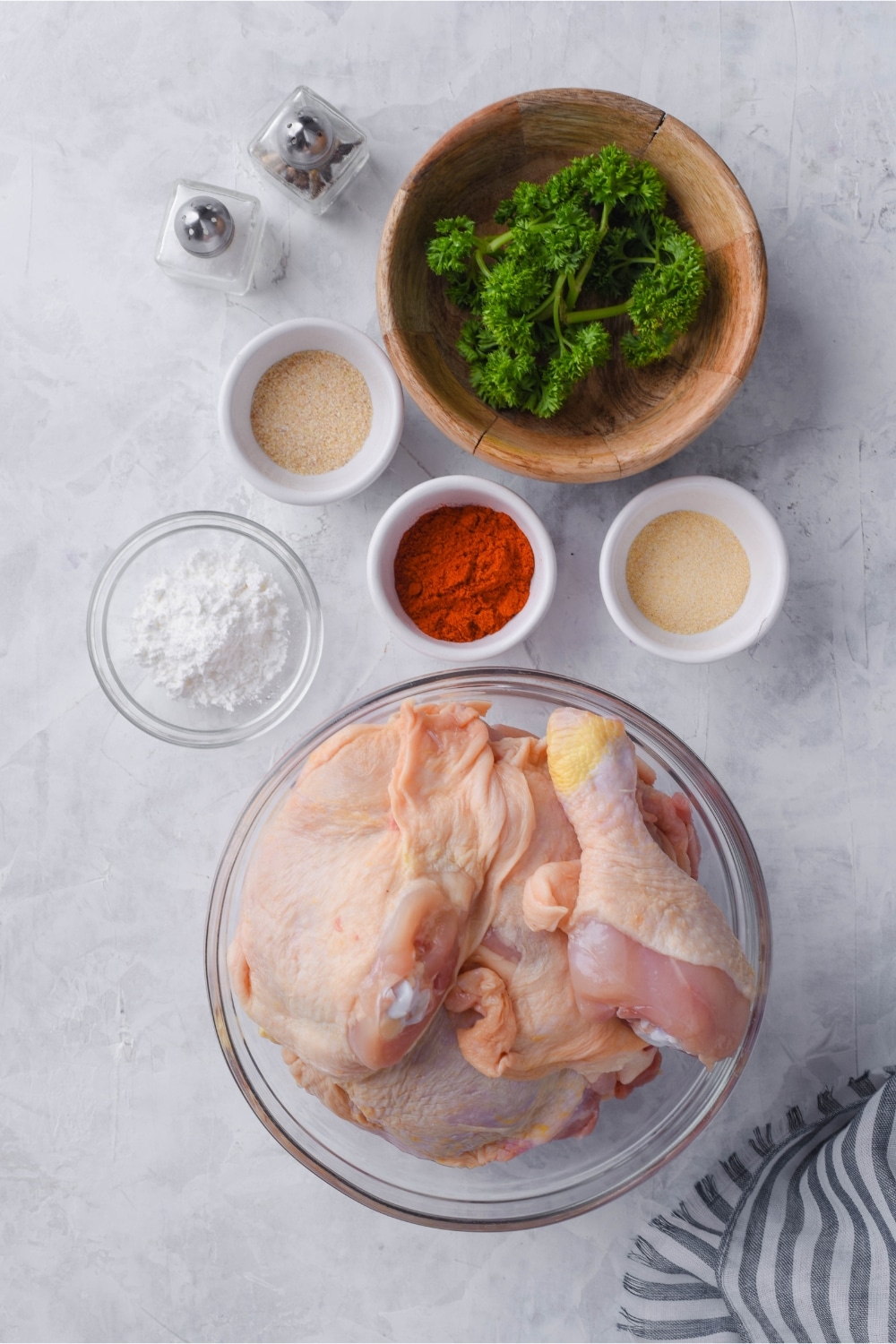 Bowls of chicken legs and thighs, seasonings and baking powder, curly parsley, and salt and pepper shakers.