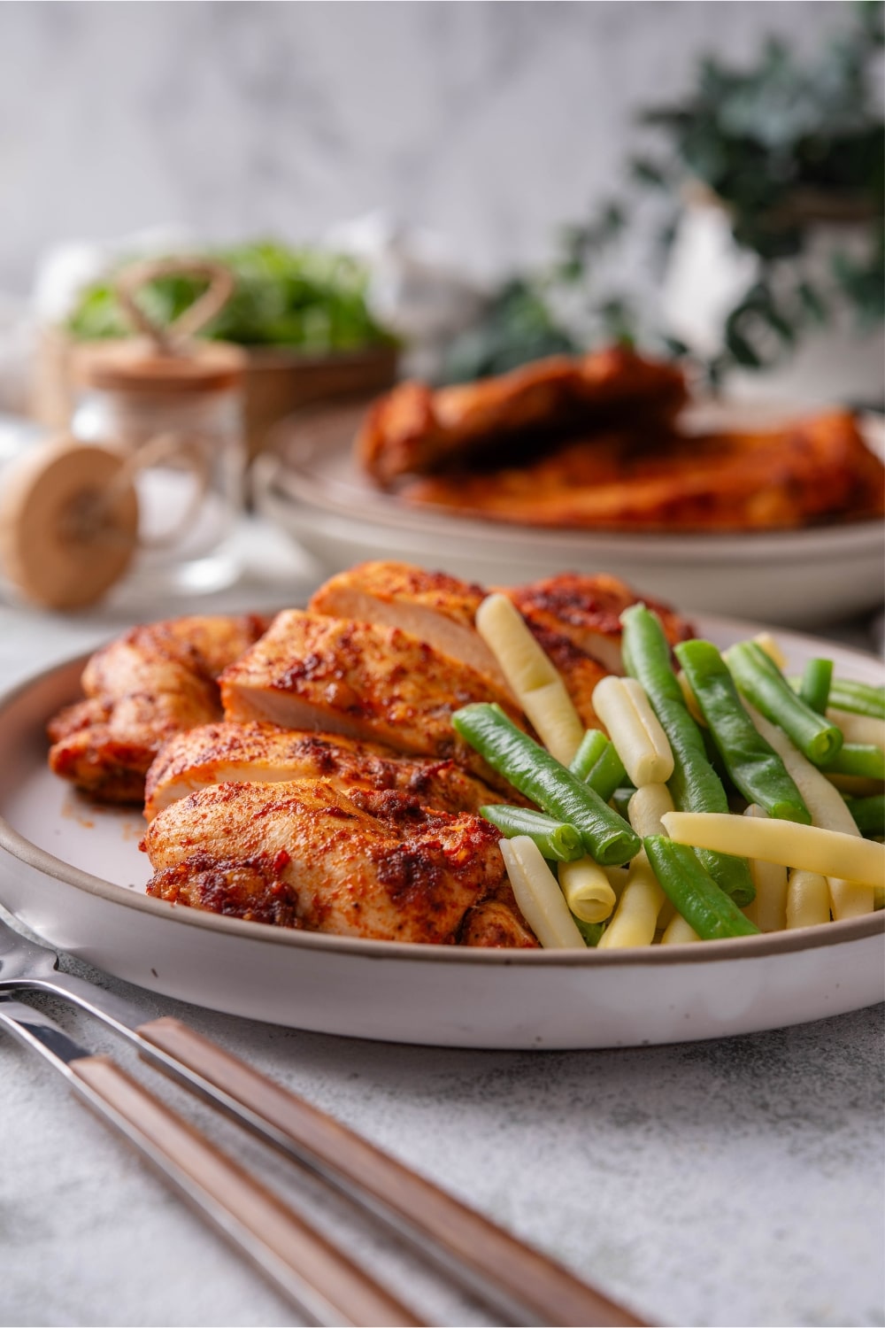 Baked thin chicken breasts on a plate served with steamed green beans.