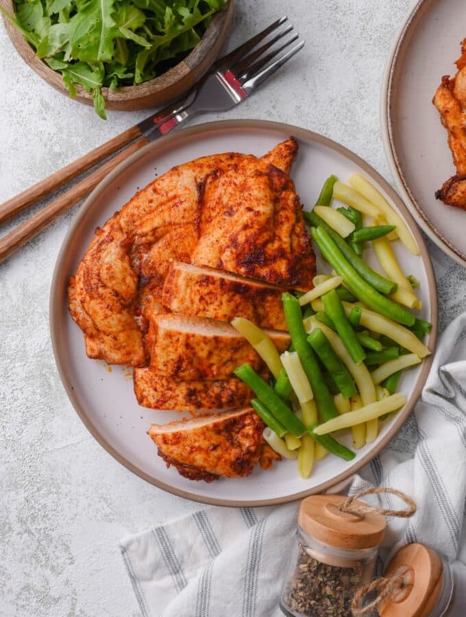 Top view of a plate of baked thin chicken breasts and steamed string beans.