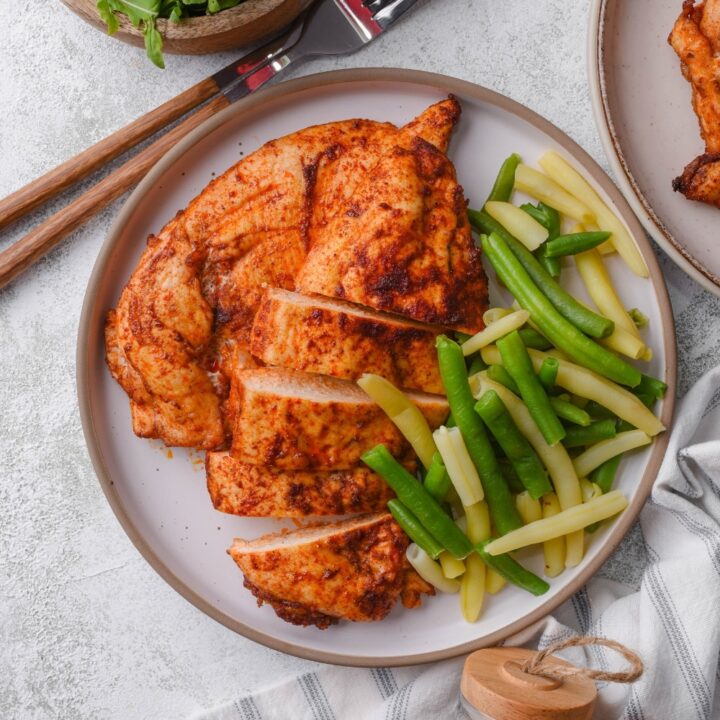 Top view of a plate of baked thin chicken breasts and steamed string beans.