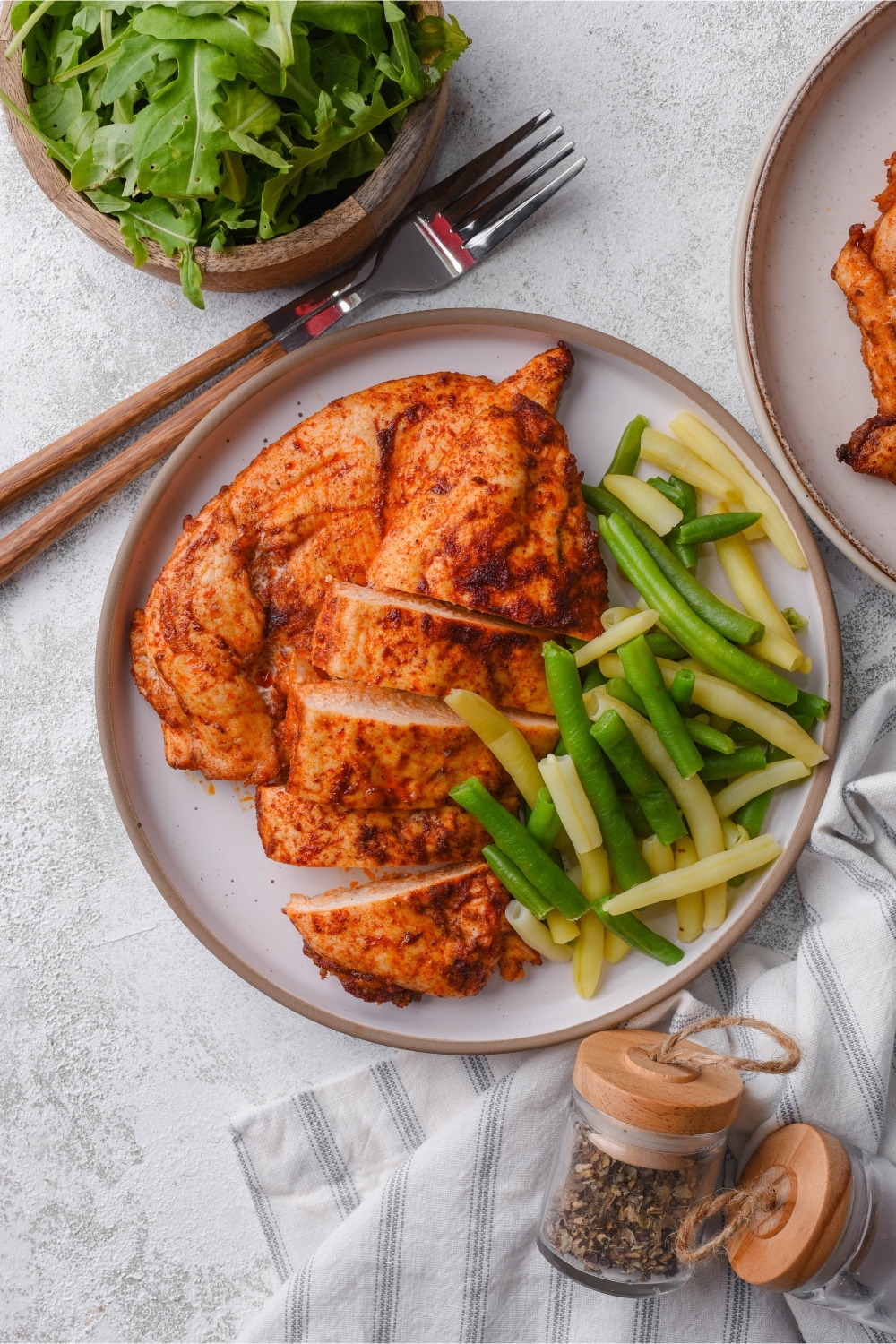 Top view of a plate of baked thin chicken breasts and steamed string beans.