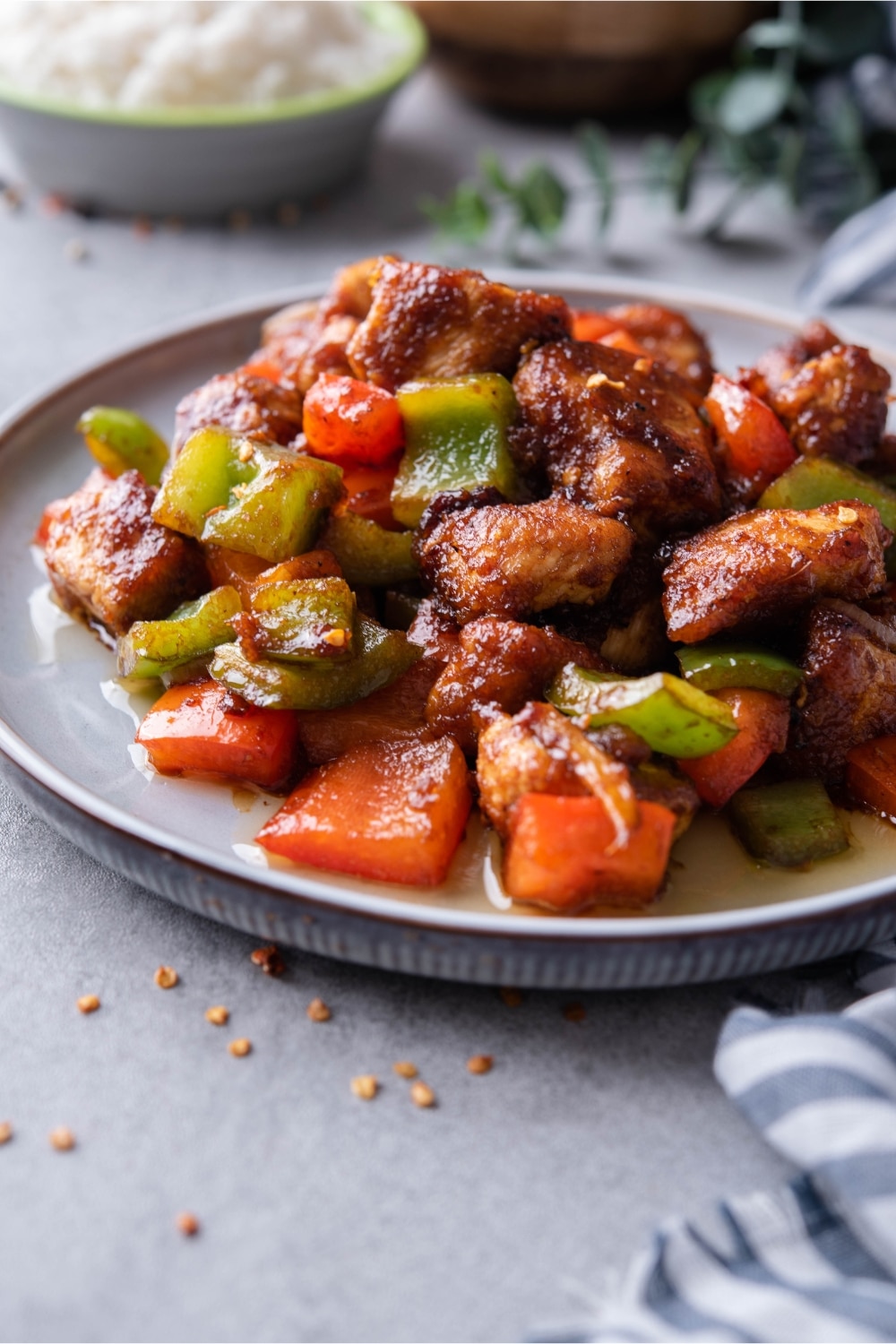 A plate of Szechuan chicken with peppers on a grayish blue table.