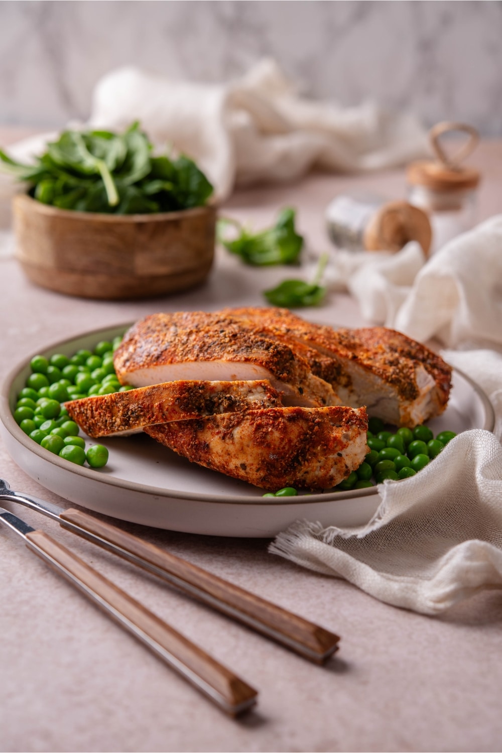 A plate of baked boneless skinless turkey breast served with green peas and a bowl of spinach.