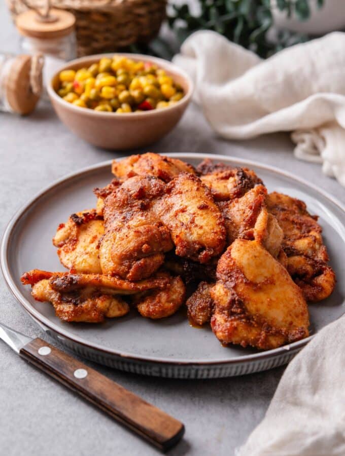 A plate of baked boneless skinless chicken thighs garnished served with a small bowl of corn and peas.