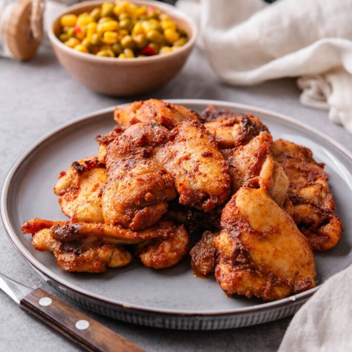 A plate of baked boneless skinless chicken thighs garnished served with a small bowl of corn and peas.