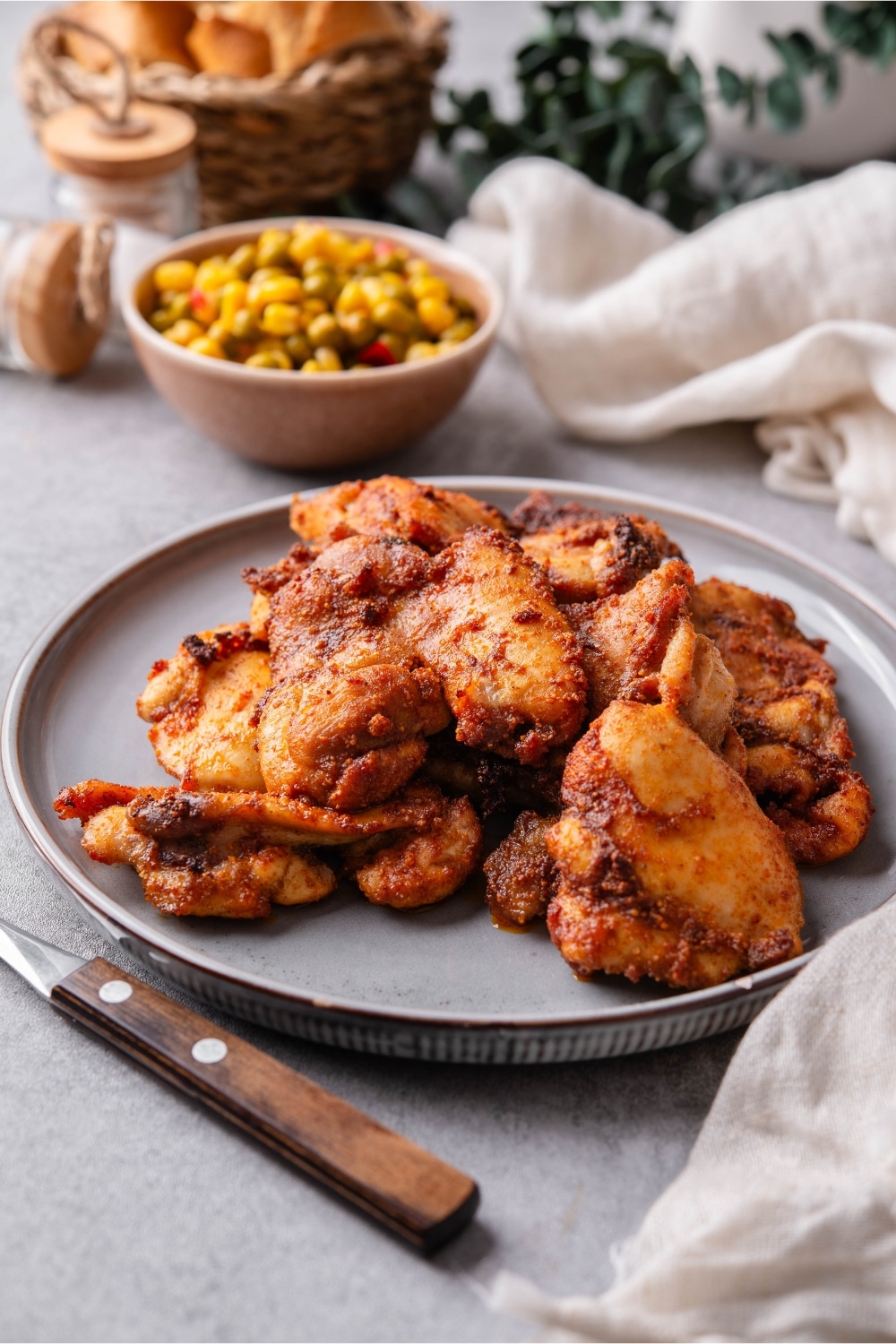 A plate of baked boneless skinless chicken thighs garnished served with a small bowl of corn and peas.