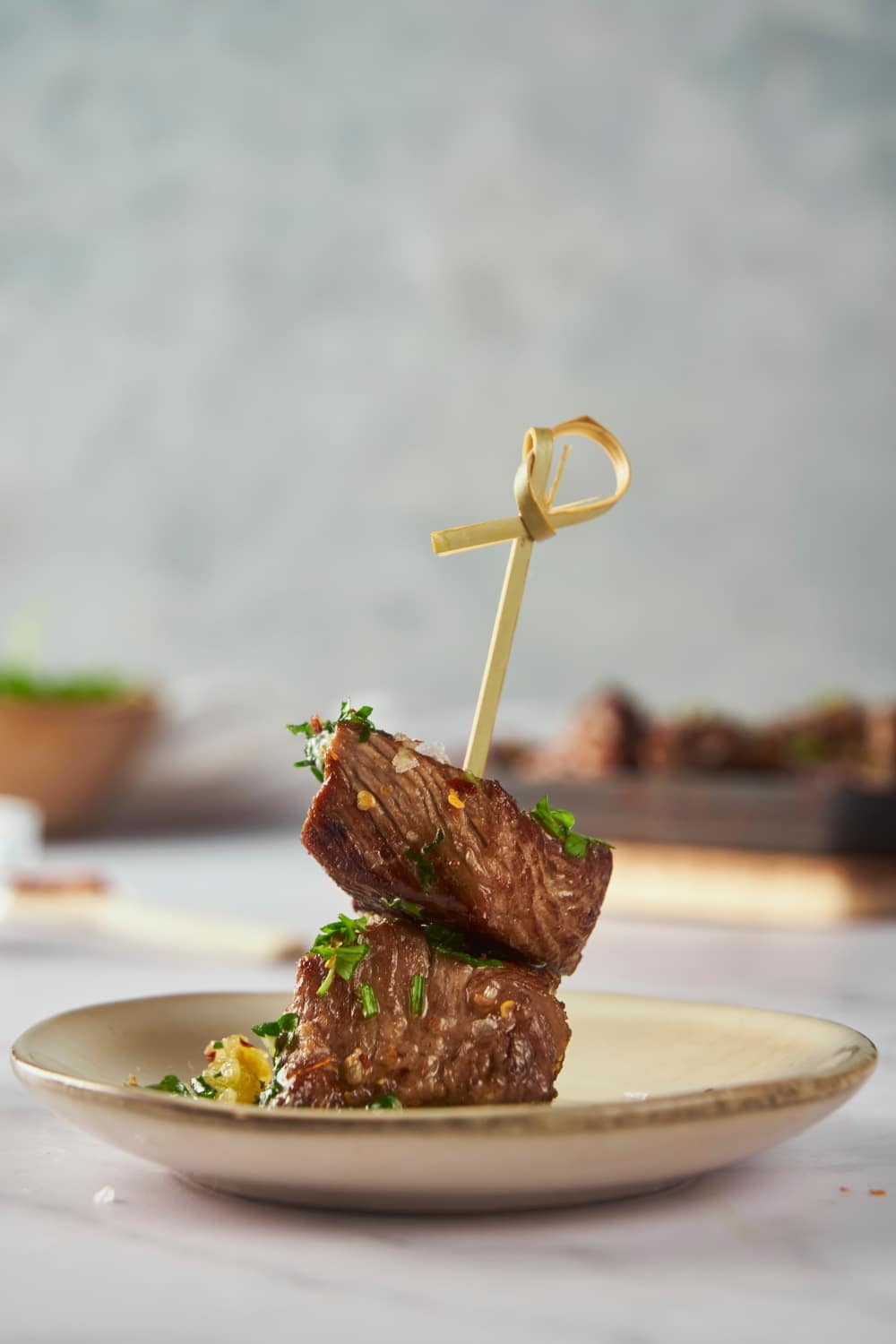 Two garlic steak bites on a gold skewer plated and garnished with parsley and red pepper flakes.
