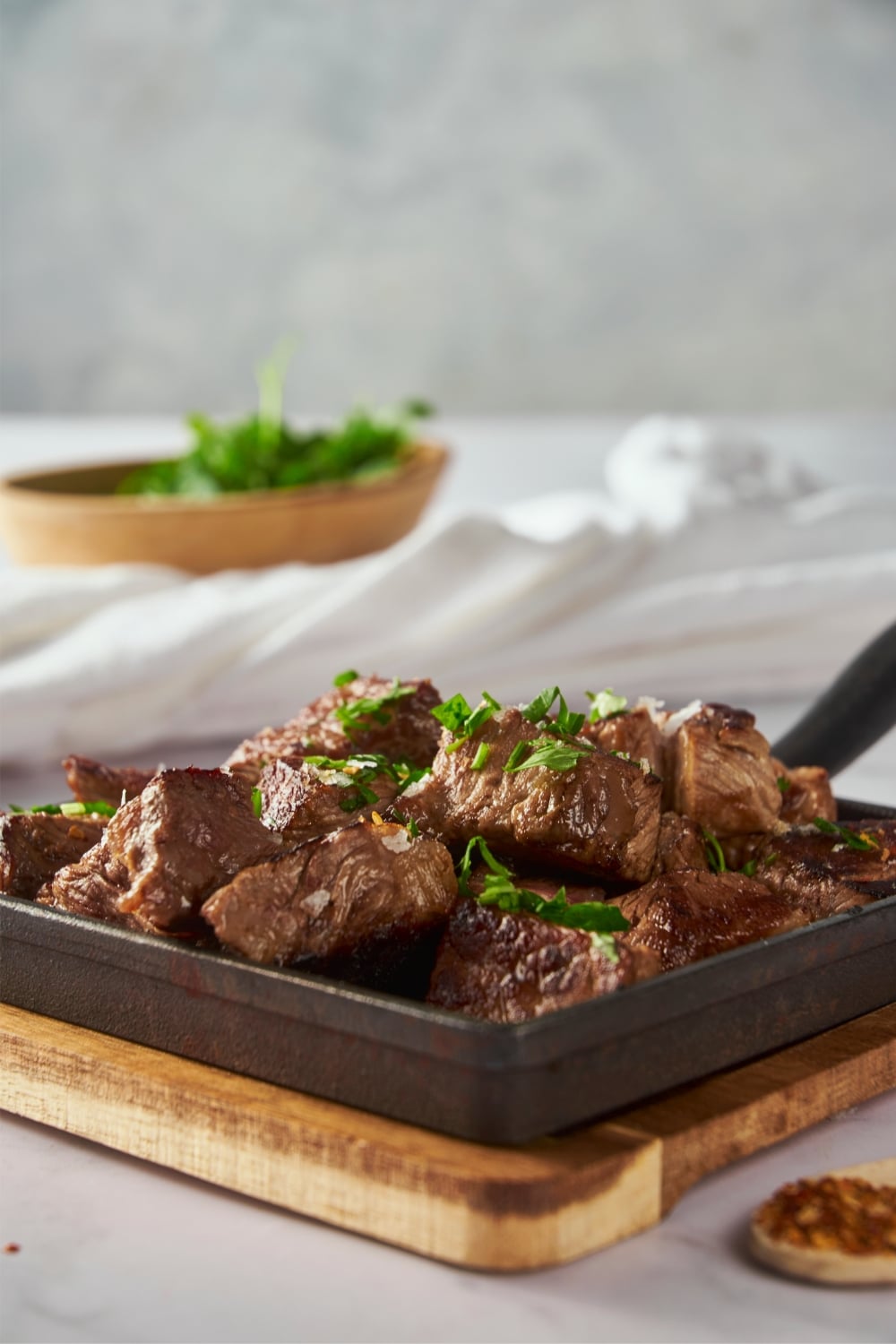 Garlic steak bites garnished with parsley on a square cast iron pan.