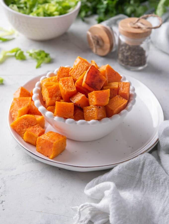 Roasted butternut squash in a white bowl on a plate.