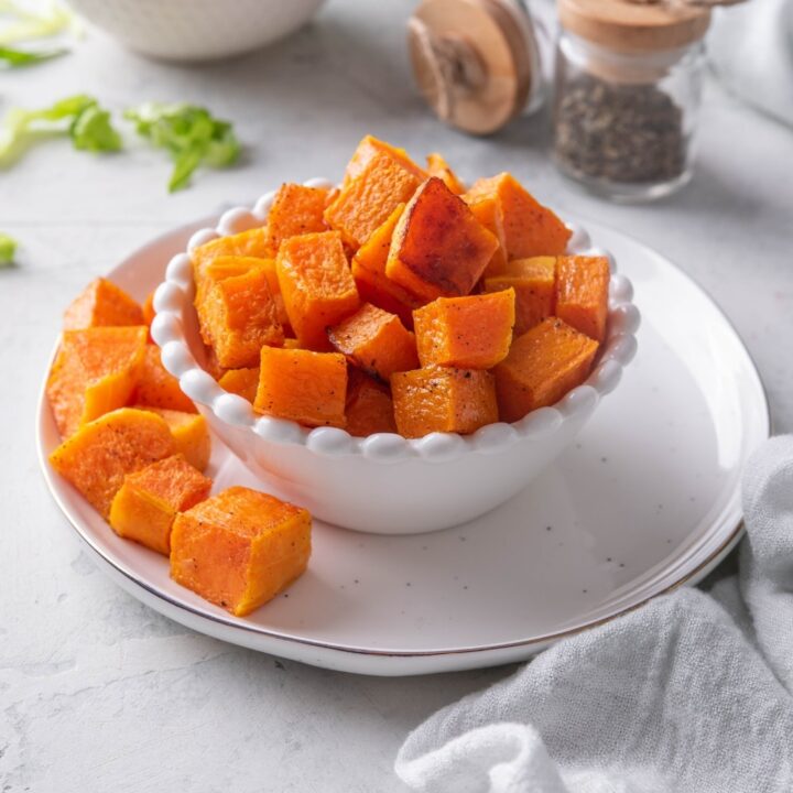 Roasted butternut squash in a white bowl on a plate.