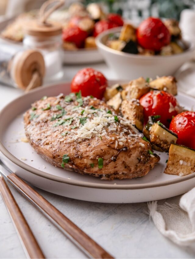 A plate of Italian baked chicken served with roasted tomatoes and zucchini.