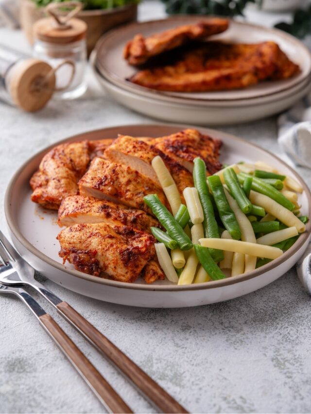 Baked thin chicken breasts and steamed green beans on a plate. Next to it is another plate of baked thin chicken breasts.