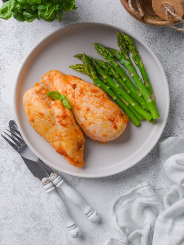 Top view of a plate of baked chicken breasts served with asparagus and garnished with basil leaves.