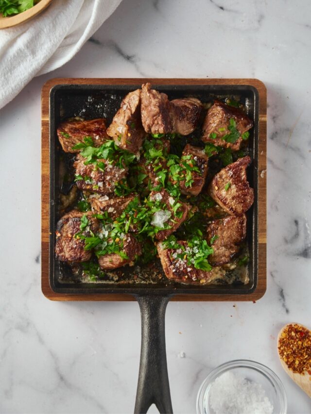 Top view garlic steak bites garnished with parsley and red pepper flakes on a square cast iron pan.