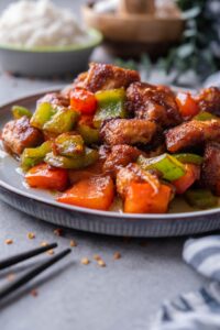 Close up of a plate of Szechuan chicken with peppers served with chopsticks.