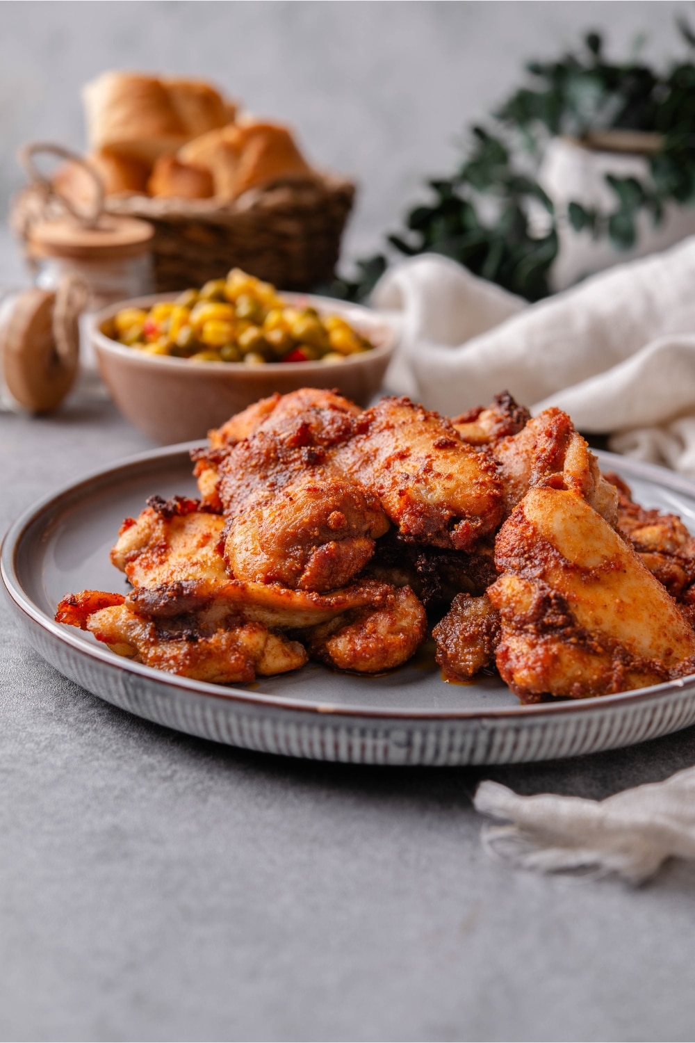 Baked boneless skinless chicken thighs garnished on a plate and served with a small bowl of corn and peas on the side.