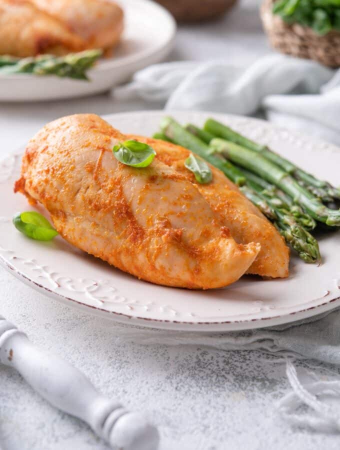 Seasoned baked chicken breasts served with asparagus and garnished with basil leaves on a plate.