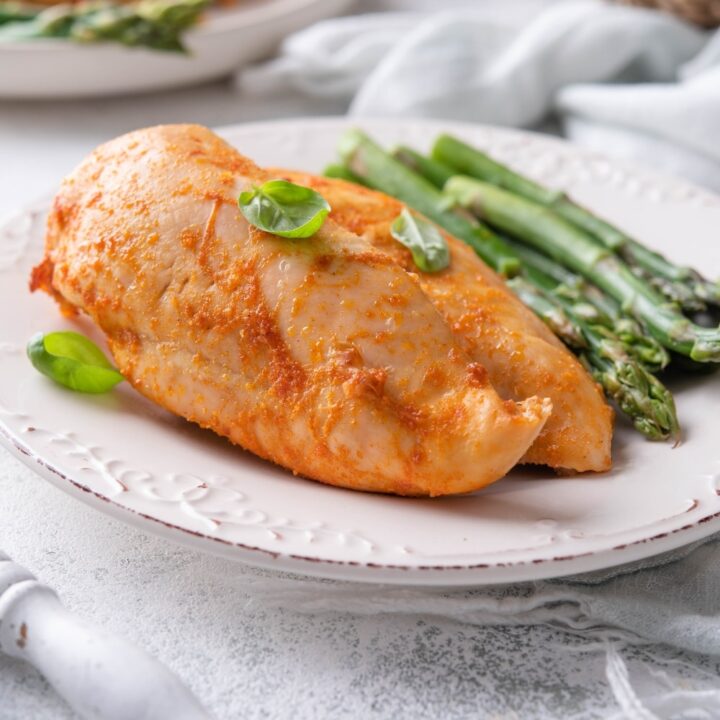 Seasoned baked chicken breasts served with asparagus and garnished with basil leaves on a plate.