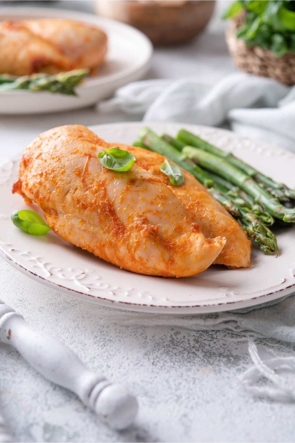 Seasoned baked chicken breasts served with asparagus and garnished with basil leaves on a plate.