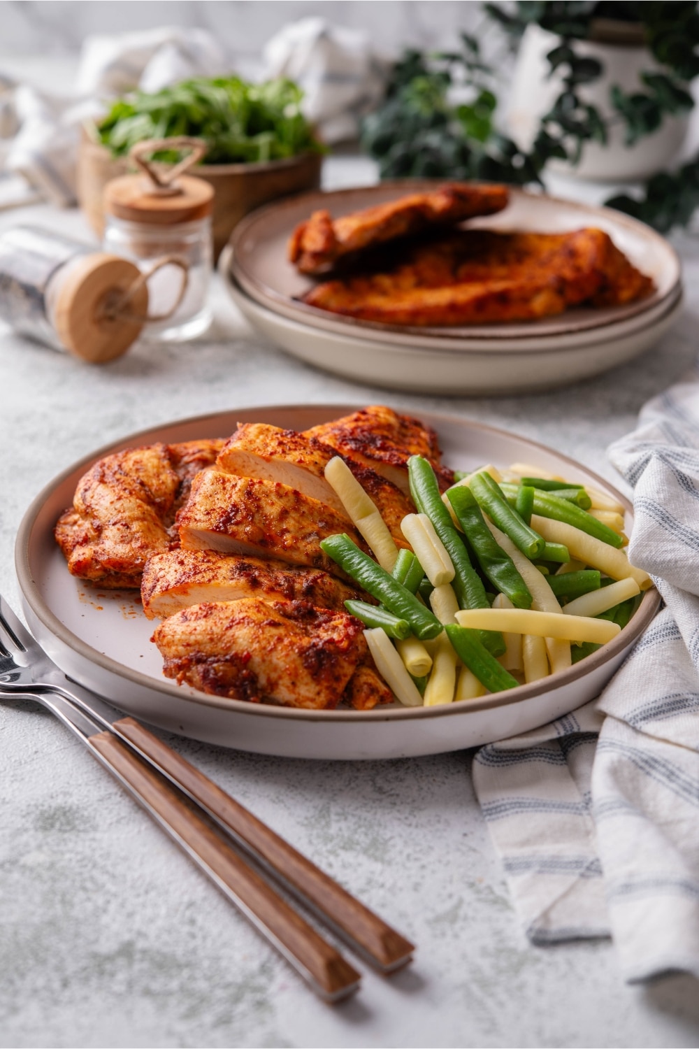 Baked thin chicken breasts and steamed green and yellow string beans on a plate.