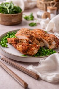 A plate of baked turkey breast sliced and served with green peas and a bowl of spinach.