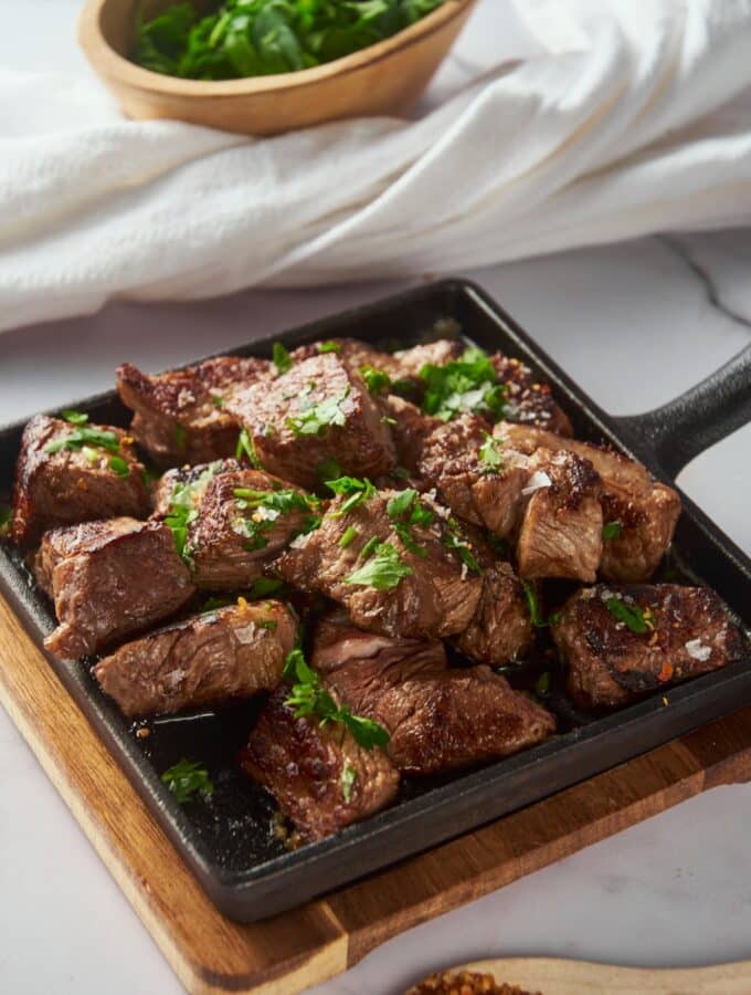 Garlic steak bites on a cast iron pan garnished with parsley.