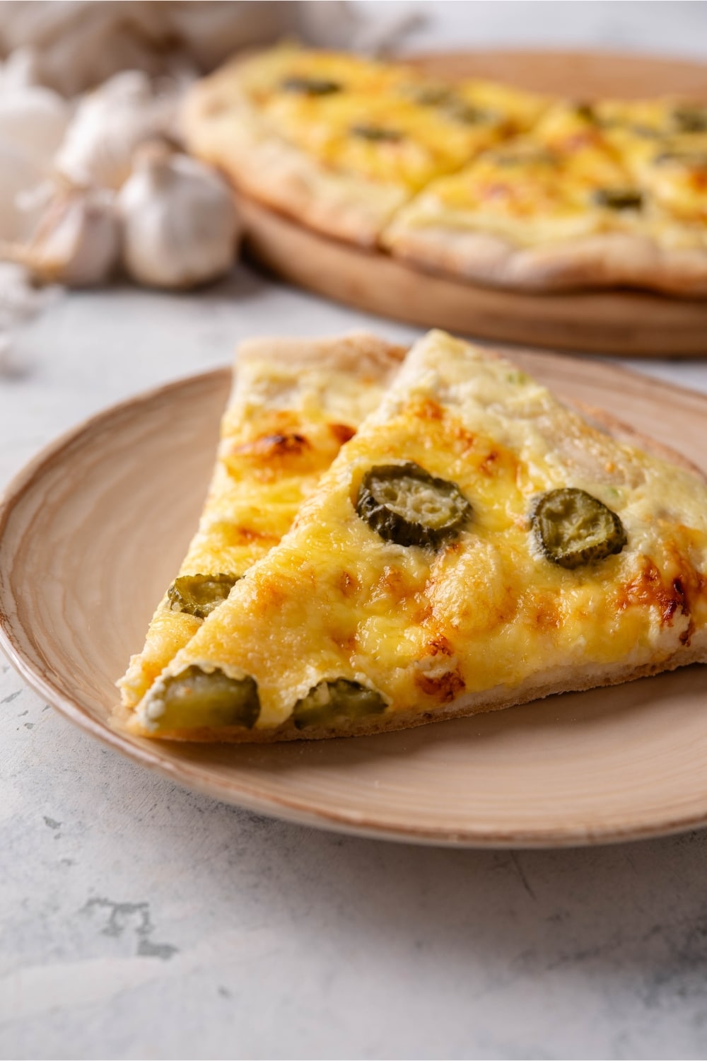 A couple of dill pickle pizza slices on a plate next to a platter with the rest of the pizza.