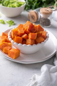 Cubed roasted butternut squash in a white bowl on a plate.