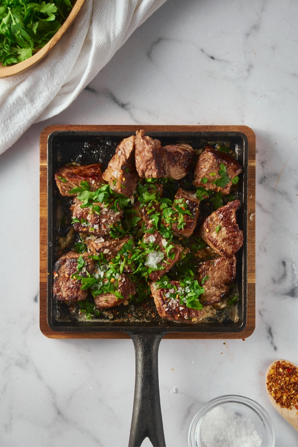 Top view garlic steak bites garnished with parsley and red pepper flakes on a square cast iron pan.