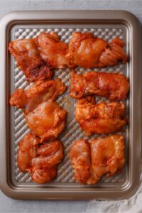 Seasoned raw boneless skinless chicken thighs on a baking sheet.